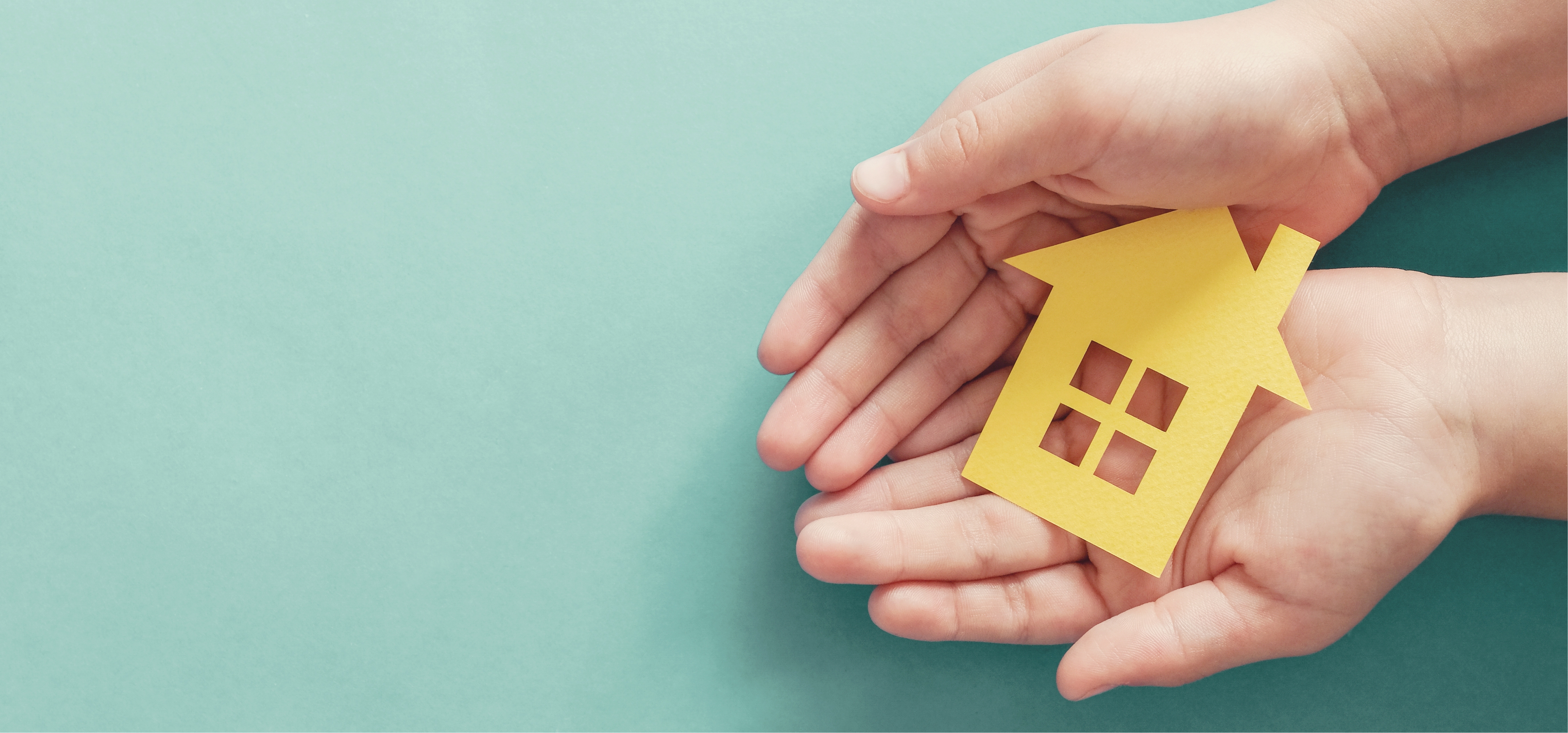 Helping hands holding a picture cut out of a home.